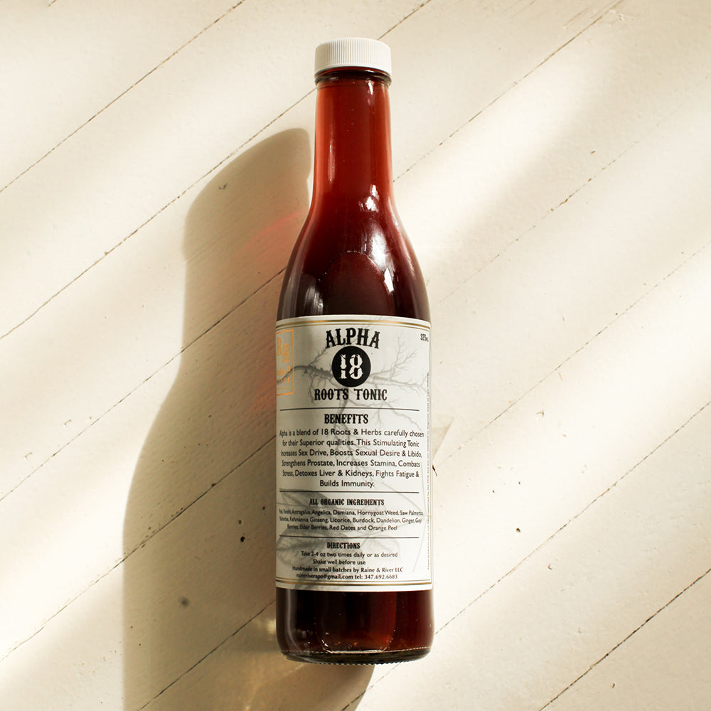 Alpha 18 Roots Tonic. Small red bottle with white label with black text and a double gold border. An overlay of roots shows on the label. The bottle sits on a light wooden background with a drop shadow going to the bottom left.